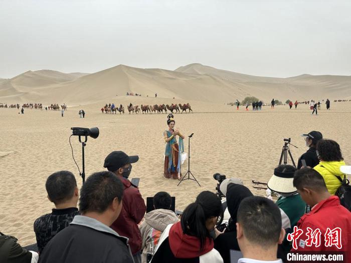 圖為2023年4月底，敦煌大漠“逐舞者”奧楠在鳴沙山月牙泉景區(qū)視頻直播，吸引游人圍觀?！●T志軍 攝
